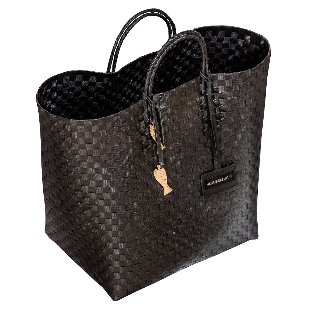 Handwoven black Theresa Bag by Adele Dejak, crafted from recycled plastic with a checkered pattern, featuring dual handles and adorned with signature brass charms, symbolizing sustainable African elegance-side angle view