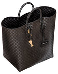 Handwoven black Theresa Bag by Adele Dejak, crafted from recycled plastic with a checkered pattern, featuring dual handles and adorned with signature brass charms, symbolizing sustainable African elegance-side angle view